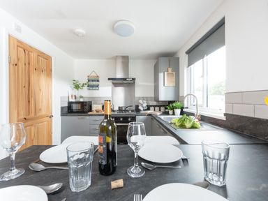 A kitchen with a dining table set with plates glasses and a bottle of wine at Wheal Prosper Lodge Wendron near Helston
