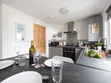 A kitchen with a dining table set with plates glasses a wine bottle and vegetables on the counter at Wheal Prosper Lodge Wendron near Helston