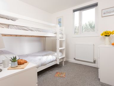 A bedroom with white bunk beds a window a white dresser with yellow flowers and a small plant with a croissant on a table at Wheal Rose Lodge in Wendron near Helston