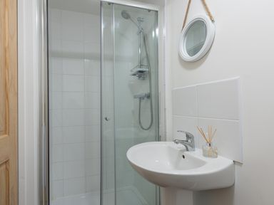 A bathroom with a shower enclosure a white sink with a faucet and a round mirror hanging on the wall at Wheal Rose Lodge in Wendron near Helston