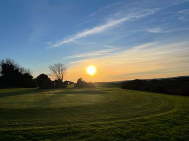 A golf green with a flag on a hole during sunset with trees in the background at Wheal Rose Lodge in Wendron near Helston