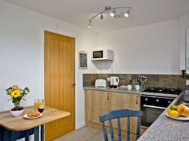 A kitchen with a wooden table holding a vase of flowers croissants and drinks near a wooden door at Wheal Tor Lodge in Wendron near Helston