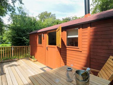 A wooden deck with a table and chairs outside a wooden hut at The Foxes Den Shepherds Hut in Oldbury-On-Severn