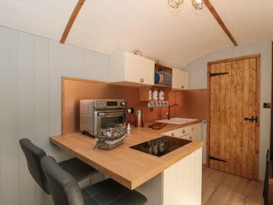 A kitchen with wooden countertops and cabinets two black chairs a metal toaster oven and a wooden door at The Foxes Den Shepherds Hut in Oldbury-On-Severn