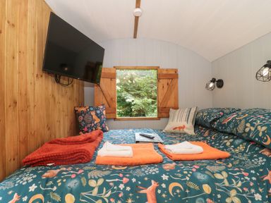 A bedroom with a bed featuring animal and nature patterned bedding and towels by a window at The Foxes Den Shepherds Hut in Oldbury-On-Severn