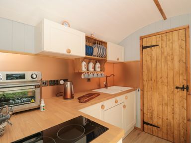 A kitchen with wooden countertops white cabinets a toaster oven kettle a sink and wooden door at The Foxes Den Shepherds Hut Oldbury-On-Severn