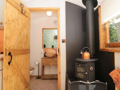 A bathroom with wooden sink cabinet and a black stove with a kettle next to a window at The Foxes Den Shepherds Hut in Oldbury-On-Severn