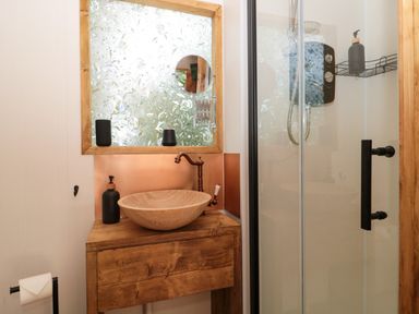 A bathroom with a wooden sink cabinet and round stone basin with a faucet next to a glass shower at The Foxes Den Shepherds Hut in Oldbury-On-Severn