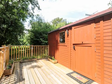 A wooden deck with plants and a red wooden door with a window at The Foxes Den Shepherds Hut in Oldbury-On-Severn