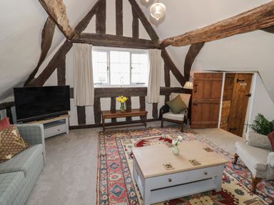 A living room with wooden beams a television sofas a coffee table and a patterned rug at The Bindery in Broadway