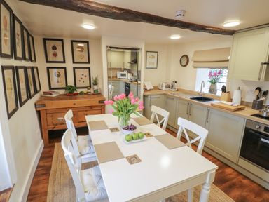 A kitchen with a white dining table and four chairs a wooden sideboard with framed pictures on the wall at The Bindery in Broadway