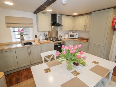 A kitchen with light green cabinets a white table with pink flowers and fruit at The Bindery in Broadway