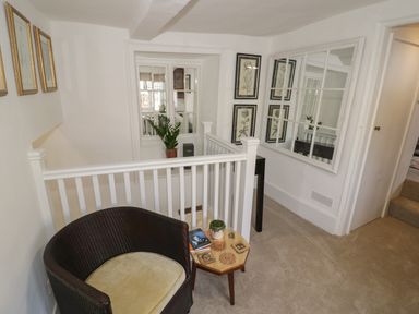 A small seating area with a wicker chair and a side table next to a white banister and botanical prints on the wall at The Bindery in Broadway