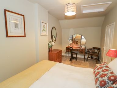 A bedroom with a bed, a wooden dresser, a vanity table with mirror and chair, a wall mirror, and framed pictures at The Bindery in Broadway