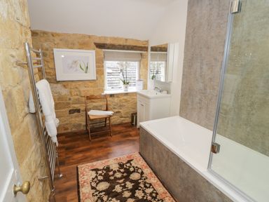 A bathroom with a bathtub shower combination a wooden chair a towel rack and a window with a flower pot at The Bindery in Broadway