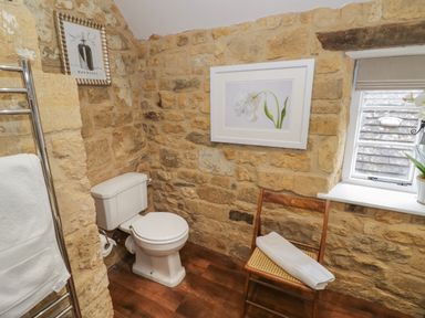 A bathroom with a toilet wooden chair with a towel stone walls and a window at The Bindery in Broadway