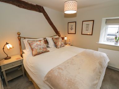 A bedroom with a double bed two bedside tables table lamps framed pictures and a window at The Bindery in Broadway
