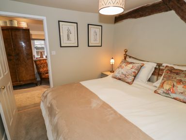 A bedroom with a bed with pillows and a beige blanket and a wooden wardrobe visible through an open door at The Bindery in Broadway