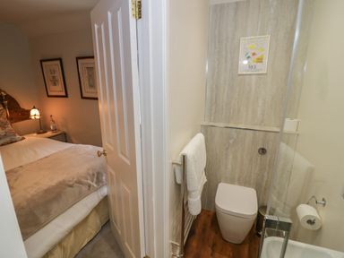 A small bedroom with a bed and side table visible through an open door next to a bathroom with a toilet towel rack and framed picture on the wall at The Bindery in Broadway