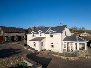 A white two-story house with dormer windows and a glass conservatory next to a stone building at Crogal Farmhouse in New Quay