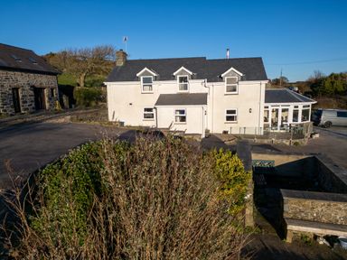 A white two-story house with dormer windows and a stone building nearby at Crogal Farmhouse in New Quay