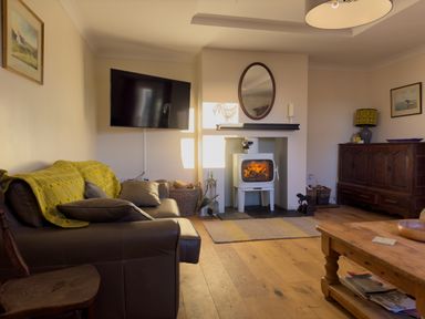 A living room with a leather sofa a mounted television a fireplace with a fire and wooden furniture at Crogal Farmhouse in New Quay