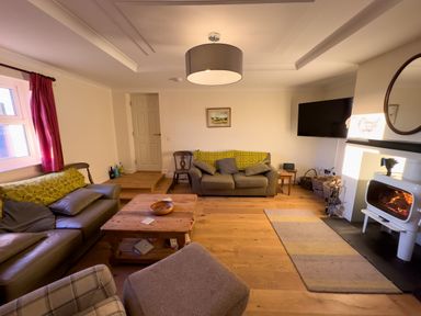 A living room with two sofas a wooden coffee table a wood burning stove and a wall mounted tv at Crogal Farmhouse in New Quay