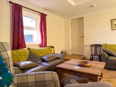 A living room with leather sofas wooden coffee table and window with red curtains at Crogal Farmhouse in New Quay