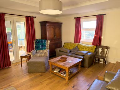 A living room with a wooden coffee table sofa armchair wooden cabinet and red curtains at Crogal Farmhouse in New Quay