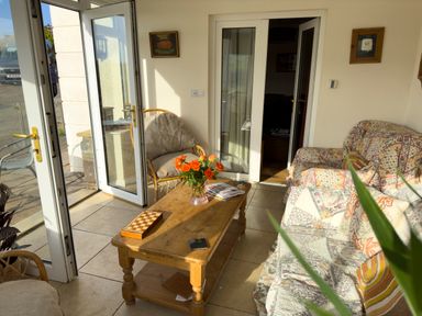 A living area with a wooden coffee table, floral couches, a plant, and open glass doors at Crogal Farmhouse in New Quay