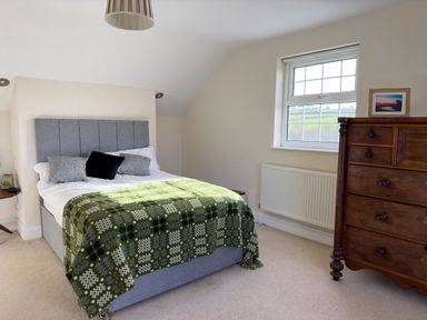 A bedroom with a bed covered by a green patterned blanket a wooden chest of drawers and a window at Crogal Farmhouse in New Quay