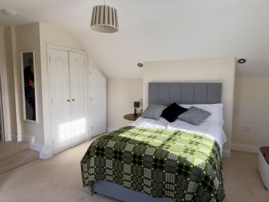 A bedroom with a bed with a green patterned blanket and pillows a round side table with a lamp and phone a double closet and a staircase with a mirror on the wall at Crogal Farmhouse in New Quay