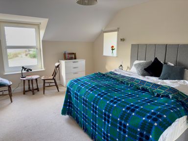 A bedroom with a bed covered with a blue and green blanket two wooden chairs a small round table and a white chest of drawers at Crogal Farmhouse in New Quay