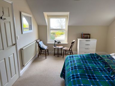 A bedroom with two wooden chairs and a small round table under a window a white chest of drawers and a bed with blue patterned blankets at Crogal Farmhouse in New Quay