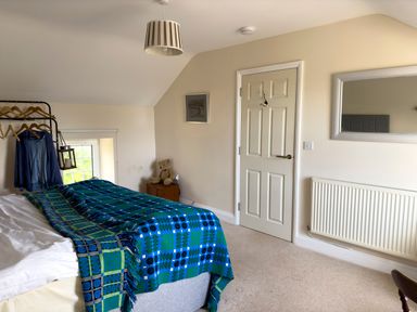 A bedroom with a bed covered with blue and green blankets a white door a mirror radiator a small wooden cabinet with a teddy bear and clothes hanging on a rack at Crogal Farmhouse in New Quay