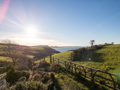A grassy hillside with wooden fences and metal wheels overlooking the sea at Crogal Farmhouse in New Quay