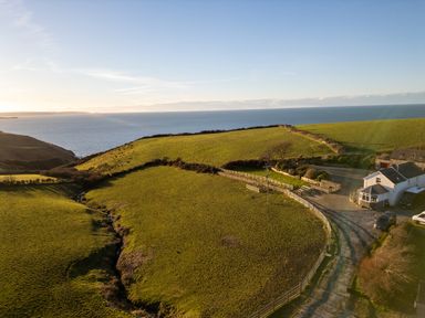 A coastal farmland with green fields and a white house near the sea at Crogal Farmhouse in New Quay