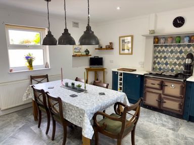 A kitchen with a dining table with candles and plants and a window with flowers on the sill at Crogal Farmhouse in New Quay