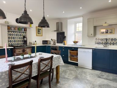 A kitchen with blue cabinets a dining table with chairs and pendant lights at Crogal Farmhouse in New Quay
