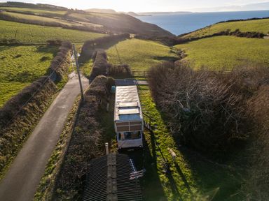 A rural landscape with a narrow road a parked camper van trees hedges and the sea in the background at Sea the Stars in New Quay