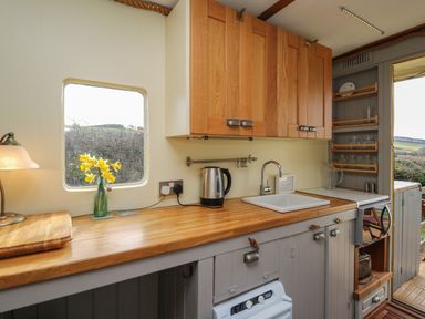 A kitchen with wooden countertops wooden cabinets a sink kettle and a window with flowers at Sea the Stars in New Quay