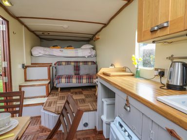 A small living space with a bunk bed, sofa, kitchen counter, kettle, and dining table at Sea the Stars in New Quay