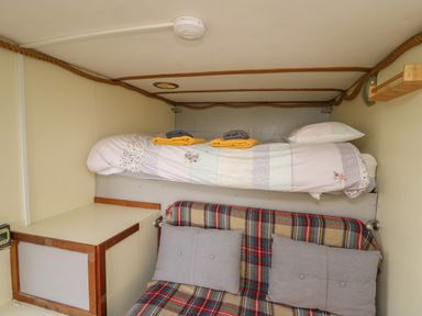 A small room with a bunk bed a plaid covered bench with cushions and a shelf at Sea the Stars in New Quay