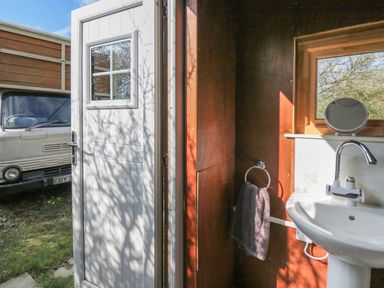 A small bathroom with a white sink towel on a ring and an open door showing a vehicle outside at Sea the Stars in New Quay