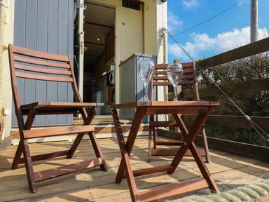 A wooden patio with two chairs a table and two wine glasses at Sea the Stars in New Quay