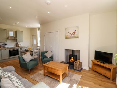 A living room and kitchen area with armchairs a coffee table a wood stove and a dining table at 2 Twizel Station Cottage in Cornhill-on-Tweed near Norham