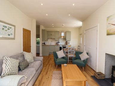 An open plan living area with a gray sofa and patterned cushions two green armchairs a wooden coffee table dining table with chairs and a kitchen with green cabinets at 2 Twizel Station Cottage Cornhill-on-Tweed near Norham