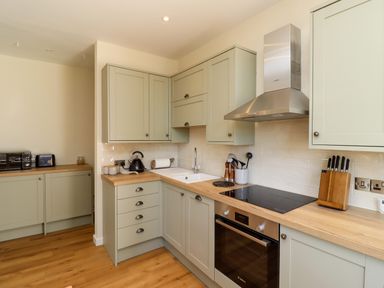 A kitchen with light green cabinets wooden countertops a stove oven and kitchen utensils at 2 Twizel Station Cottage Cornhill-on-Tweed near Norham