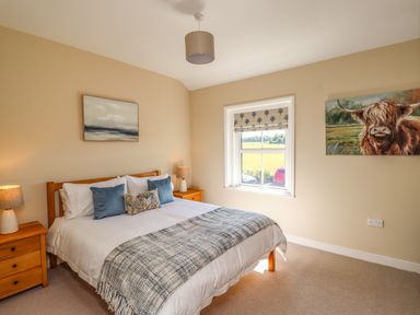 A bedroom with a double bed and bedside tables each with a lamp and a window with a Roman blind at 2 Twizel Station Cottage in Cornhill-on-Tweed near Norham