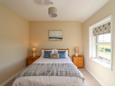 A bedroom with a double bed between two wooden bedside tables with lamps and a window at 2 Twizel Station Cottage Cornhill-on-Tweed near Norham